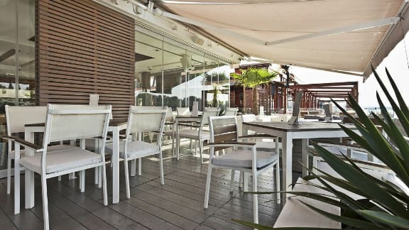 Outdoor restaurant seating shaded by a beige awning
